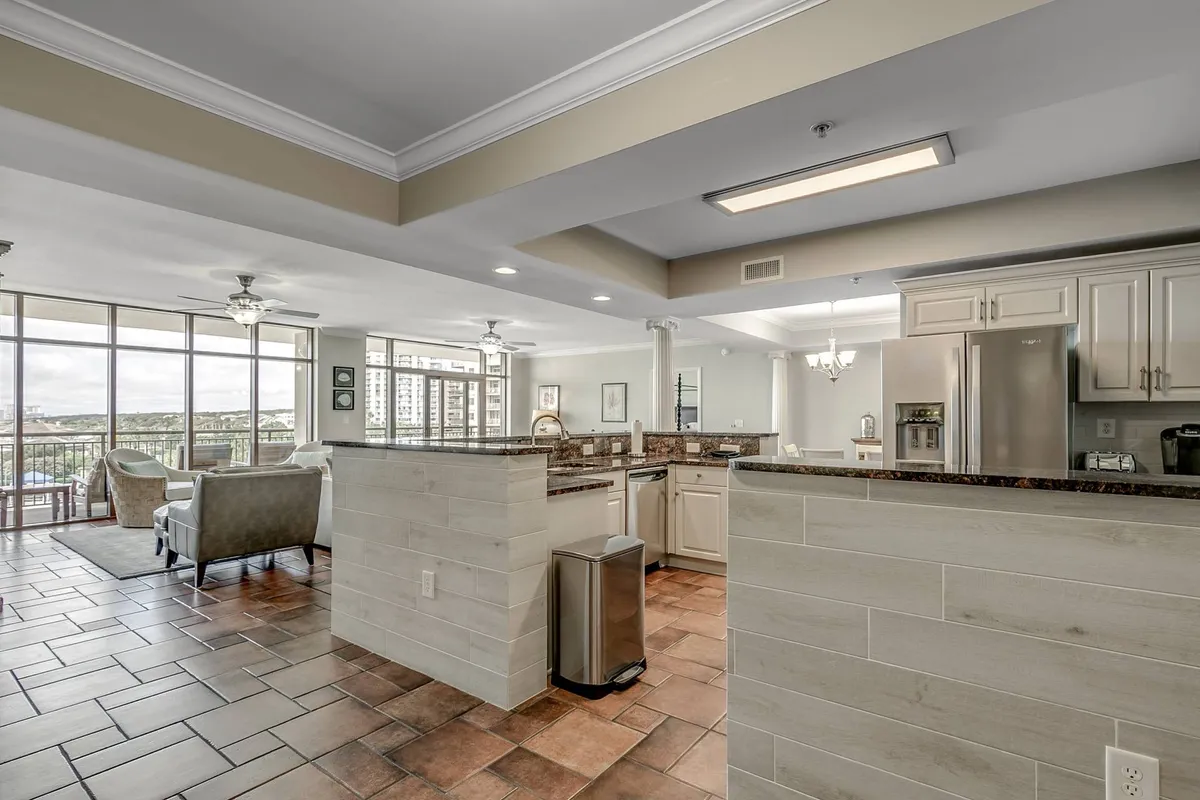 A spacious kitchen featuring a central kitchen island, large windows that bathe the room in natural light, a seating area, and modern appliances. The space feels open and functional, blending practicality with areas for relaxation and togetherness.