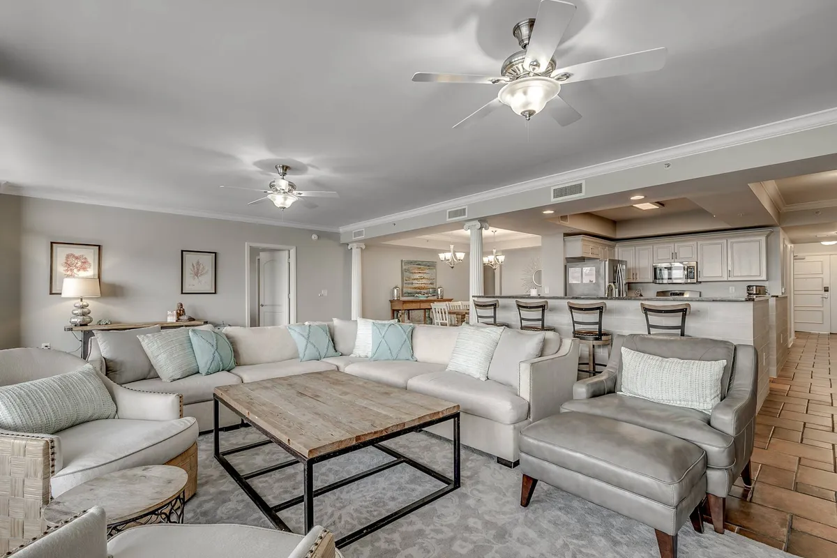 A spacious, inviting room featuring a large sectional sofa, a wooden coffee table perfect for games or snacks, a bar area with stools for socializing, and colorful decorative art on the wall. The room feels comfortable and is clearly designed for group activities, relaxation, and entertainment.