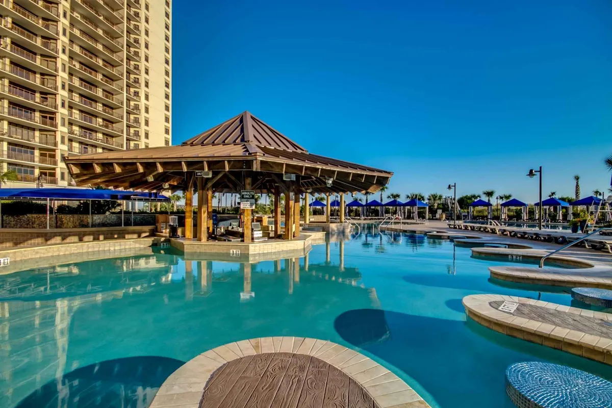 This exterior image features a sparkling resort pool surrounded by a pavilion, lounge chairs, and umbrellas, creating an inviting setting for relaxation and socializing. The scene reflects the leisurely side of North Myrtle Beach, with space for both sunbathing and group gatherings.